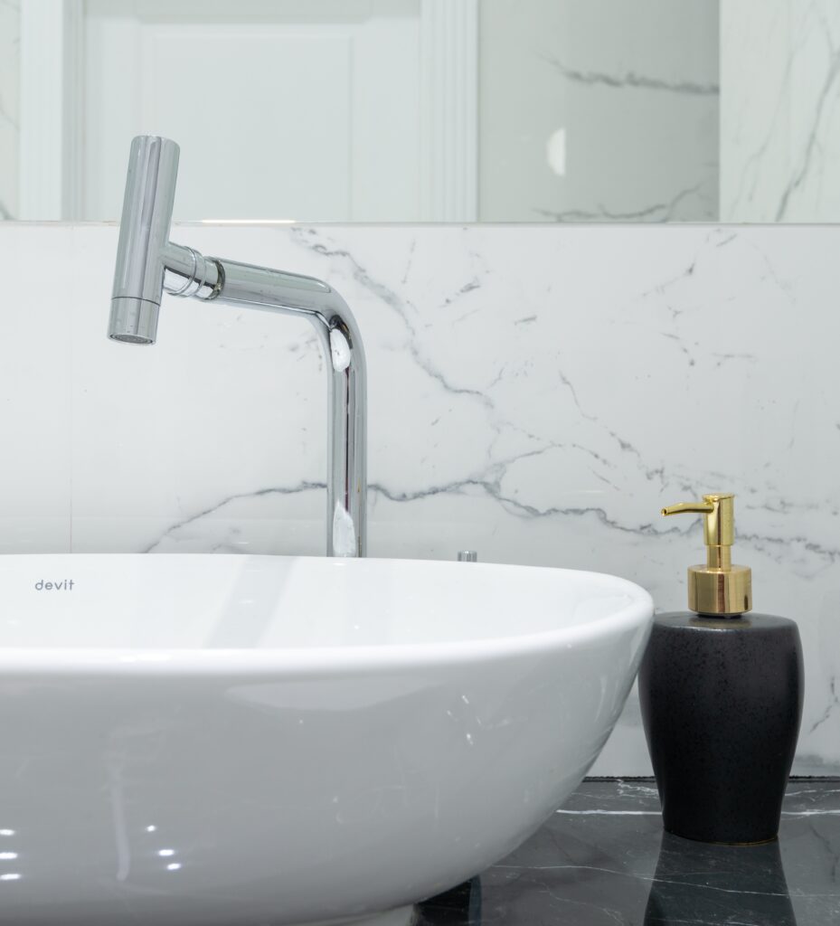 Modern bathroom sink with chrome faucet and black soap dispenser on marble countertop, highlighting plumbing fixtures relevant to Frost & Kretsch Plumbing Inc's commercial services.