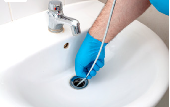 Plumber in blue gloves using a drain snake on a bathroom sink, representing efficient plumbing repair services in Roseville by Frost & Kretsch Plumbing Inc.