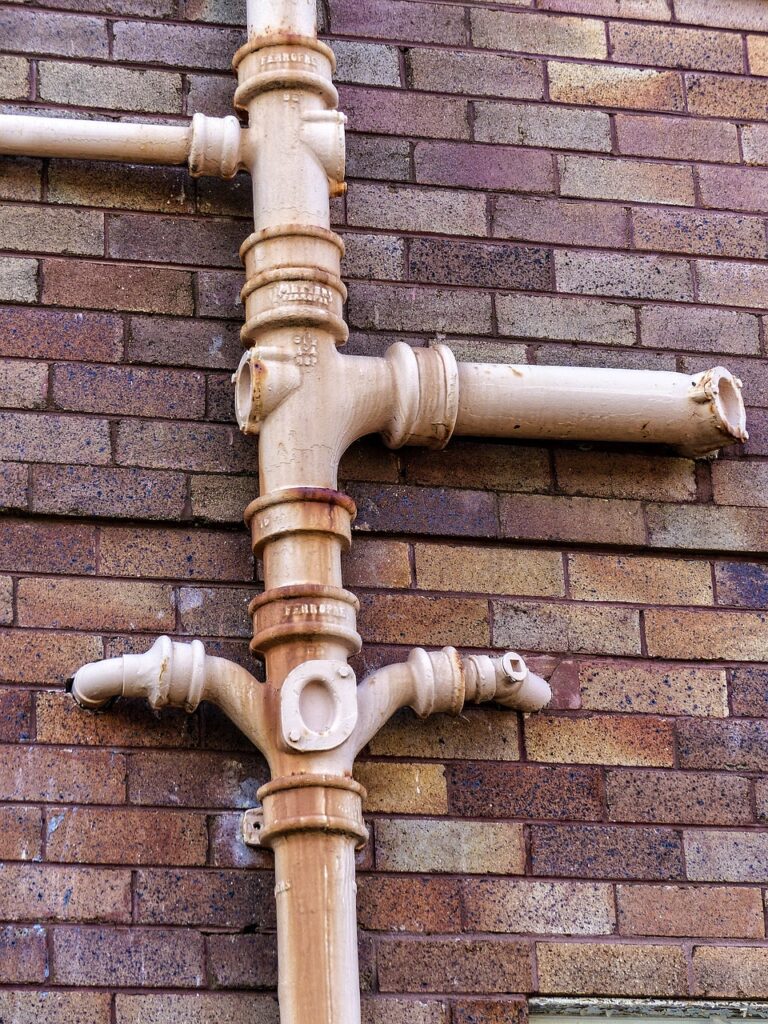 Plumbing pipes against a brick wall, illustrating plumbing infrastructure relevant to Frost & Kretsch Plumbing's services in Sterling Heights.