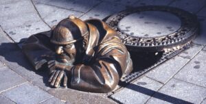 Bronze sculpture of a plumber emerging from a manhole, symbolizing plumbing expertise and service reliability, relevant to Frost & Kretsch Plumbing in Utica.